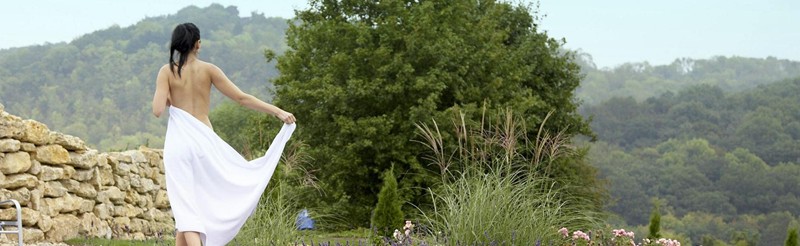 Frau im weißen Tuch genießt den Sommer im Wellnessgarten mit Blick auf die grüne Hügellandschaft in Bad Sulza